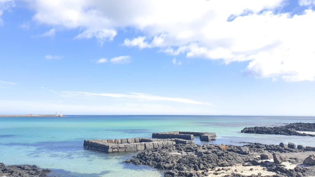 Jeju Island beach with rocky shore, emerald sea, clear horizon, and blue sky.