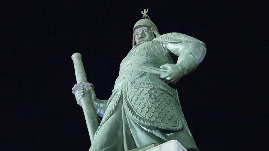 Nighttime photograph of the Admiral Yi Sun-sin statue at Gwanghwamun Square, illuminated against the dark sky.