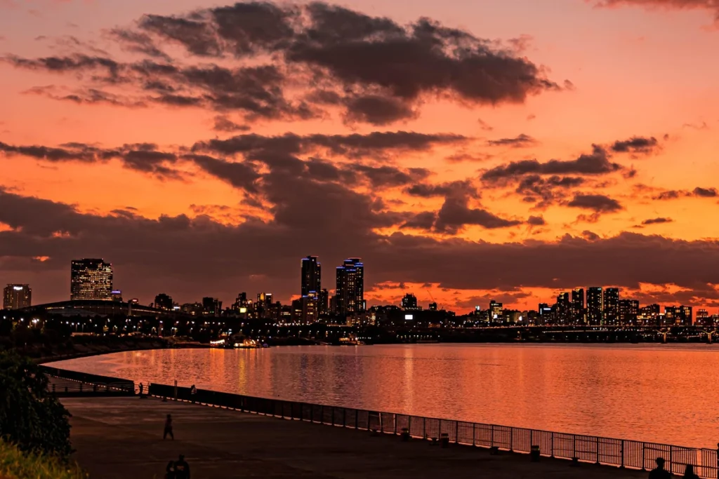 A twilight-lit alley at night, with a glowing sunset sky and a forest of buildings visible across the river.