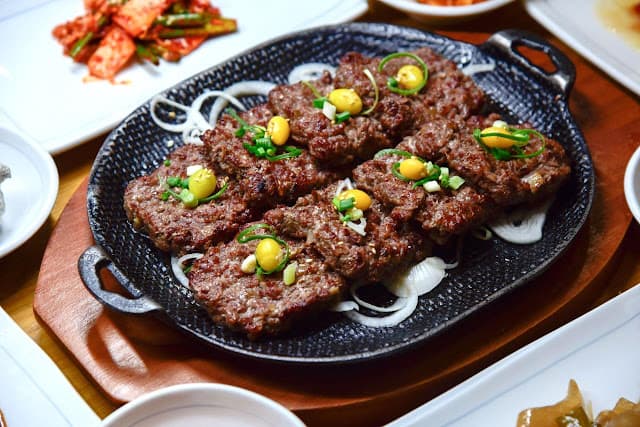 Grilled short rib patties (tteok-galbi) served on a metal plate, traditional Korean dish.