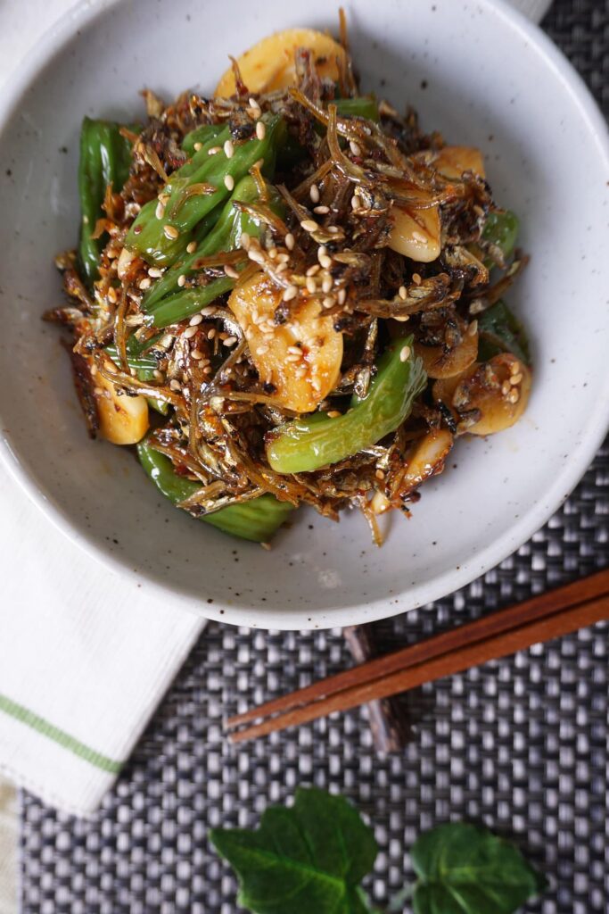 A side dish of stir-fried shishito peppers, anchovies, and sliced garlic